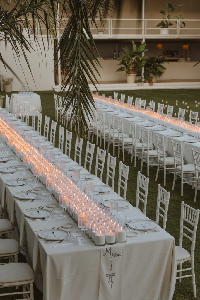 Decoración de evento en Lamarr Alicante con largas mesas iluminadas por cientos de velas blancas, diseño elegante junto a palmeras