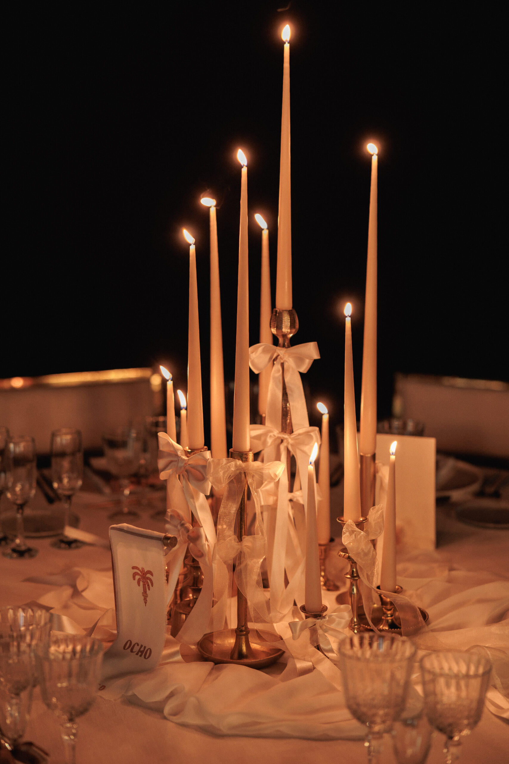Montaje de evento con alquiler de velas largas, candelabros dorados y decoración con lazos.