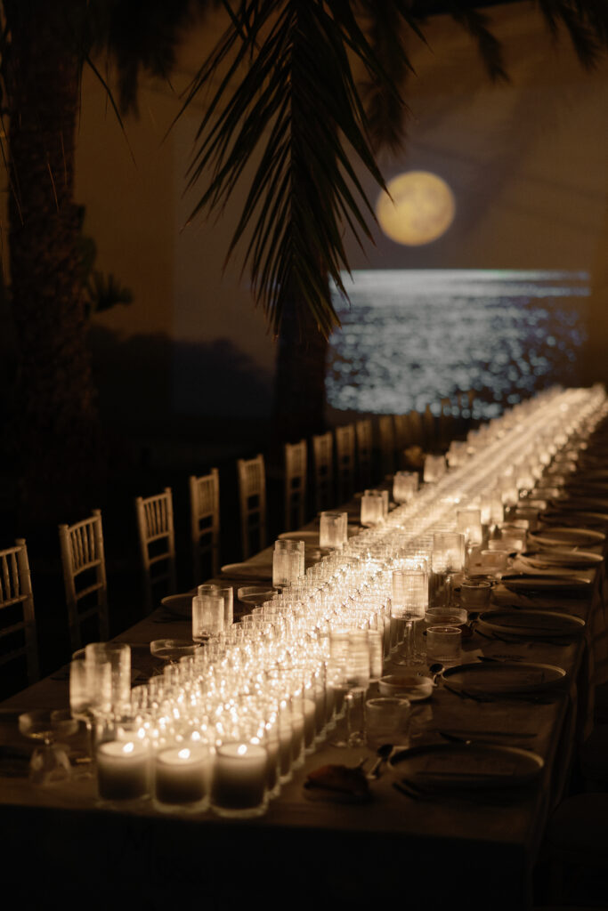 Decoración de evento en Lamarr Alicante con largas mesas iluminadas por cientos de velas blancas, diseño elegante junto a palmeras