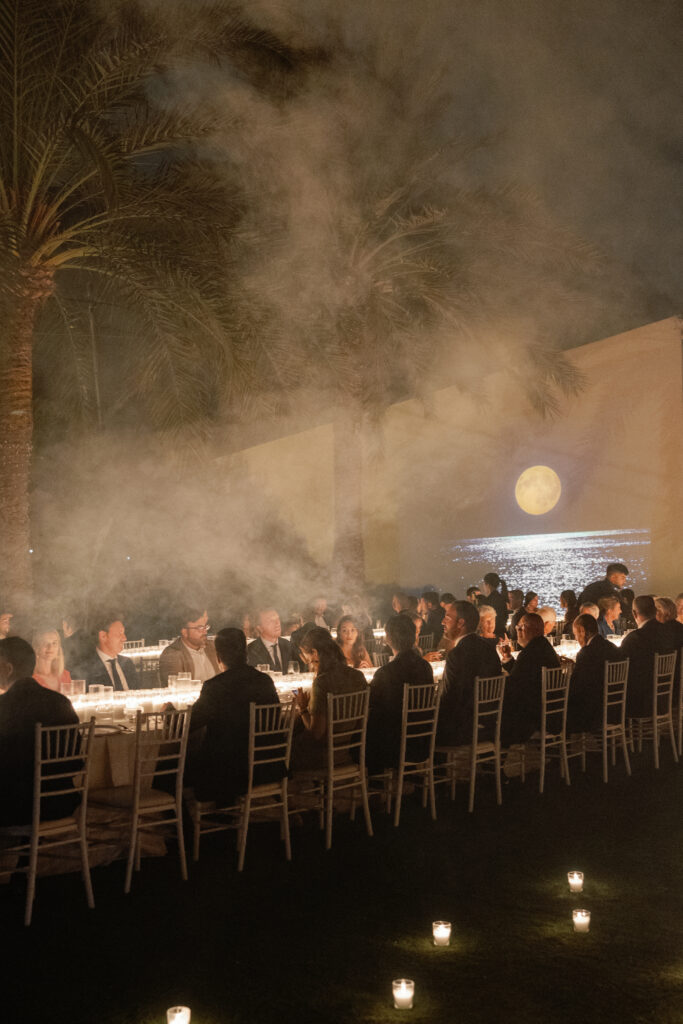 Decoración de evento en Lamarr Alicante con largas mesas iluminadas por cientos de velas blancas, diseño elegante junto a palmeras