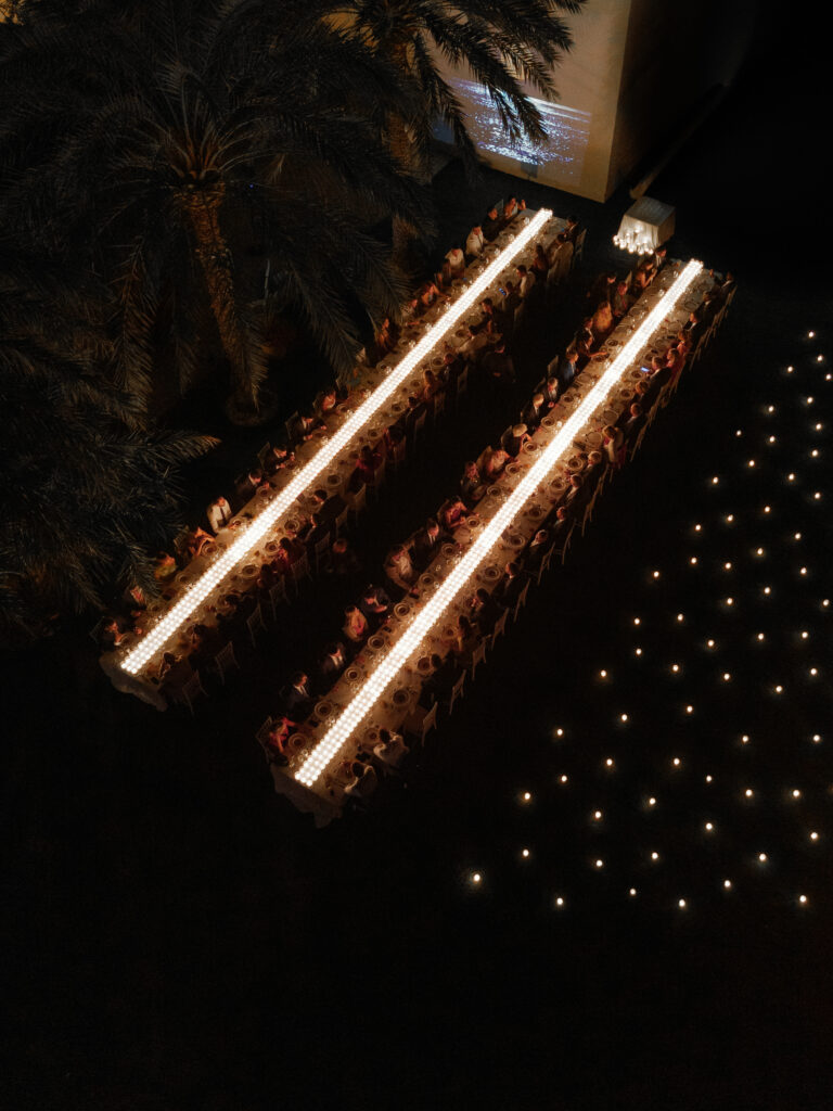 Decoración de evento en Lamarr Alicante con largas mesas iluminadas por cientos de velas blancas, diseño elegante junto a palmeras